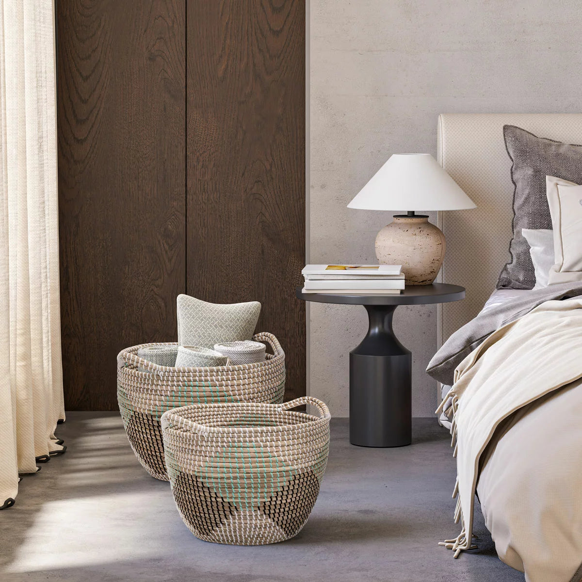 Pair of two nesting handwoven natural brown seagrass storage baskets with integrated handles arranged on a light wood floor in a brightly lit living room.
