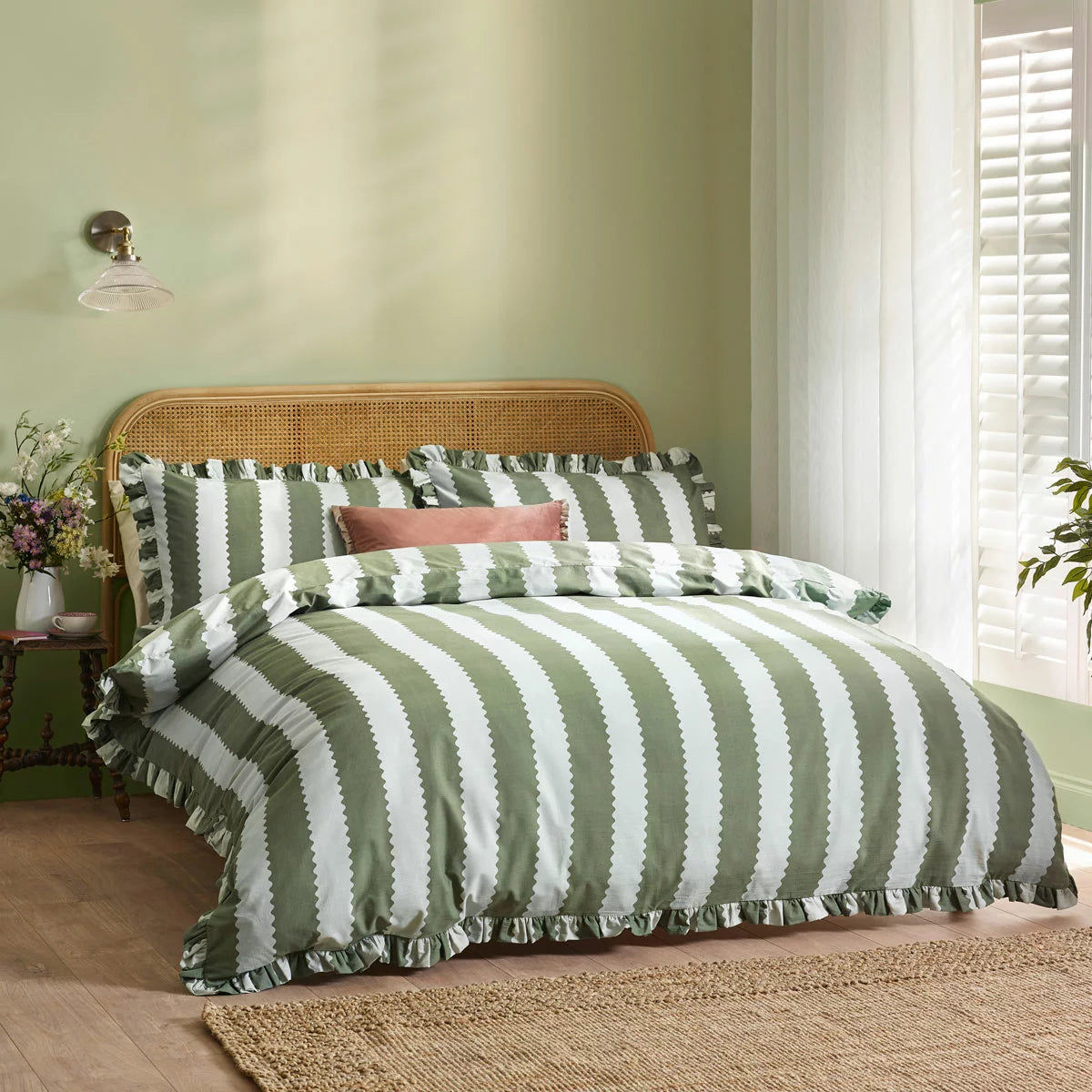 Close-up shot of the Wylder Birdie green and white striped duvet cover showing its delicate ruffled trim draped over a rustic wooden bed.