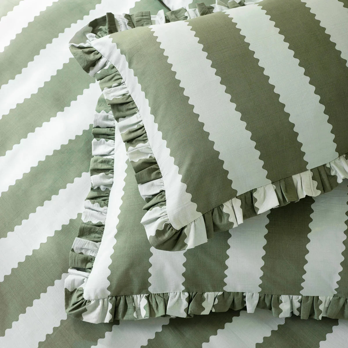 Close-up shot of the Wylder Birdie green and white striped duvet cover showing its delicate ruffled trim draped over a rustic wooden bed.