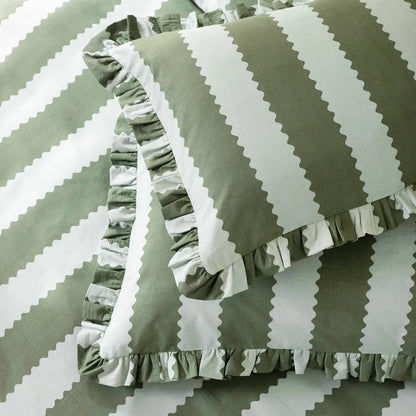 Close-up shot of the Wylder Birdie green and white striped duvet cover showing its delicate ruffled trim draped over a rustic wooden bed.