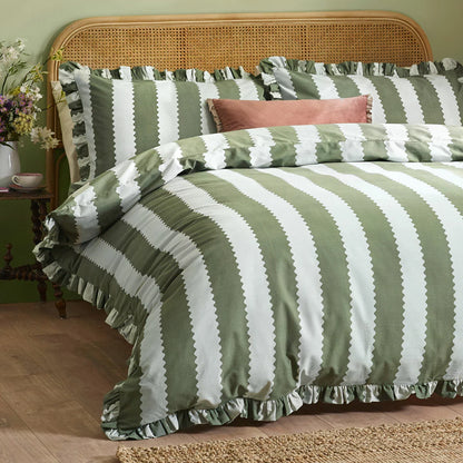Close-up shot of the Wylder Birdie green and white striped duvet cover showing its delicate ruffled trim draped over a rustic wooden bed.