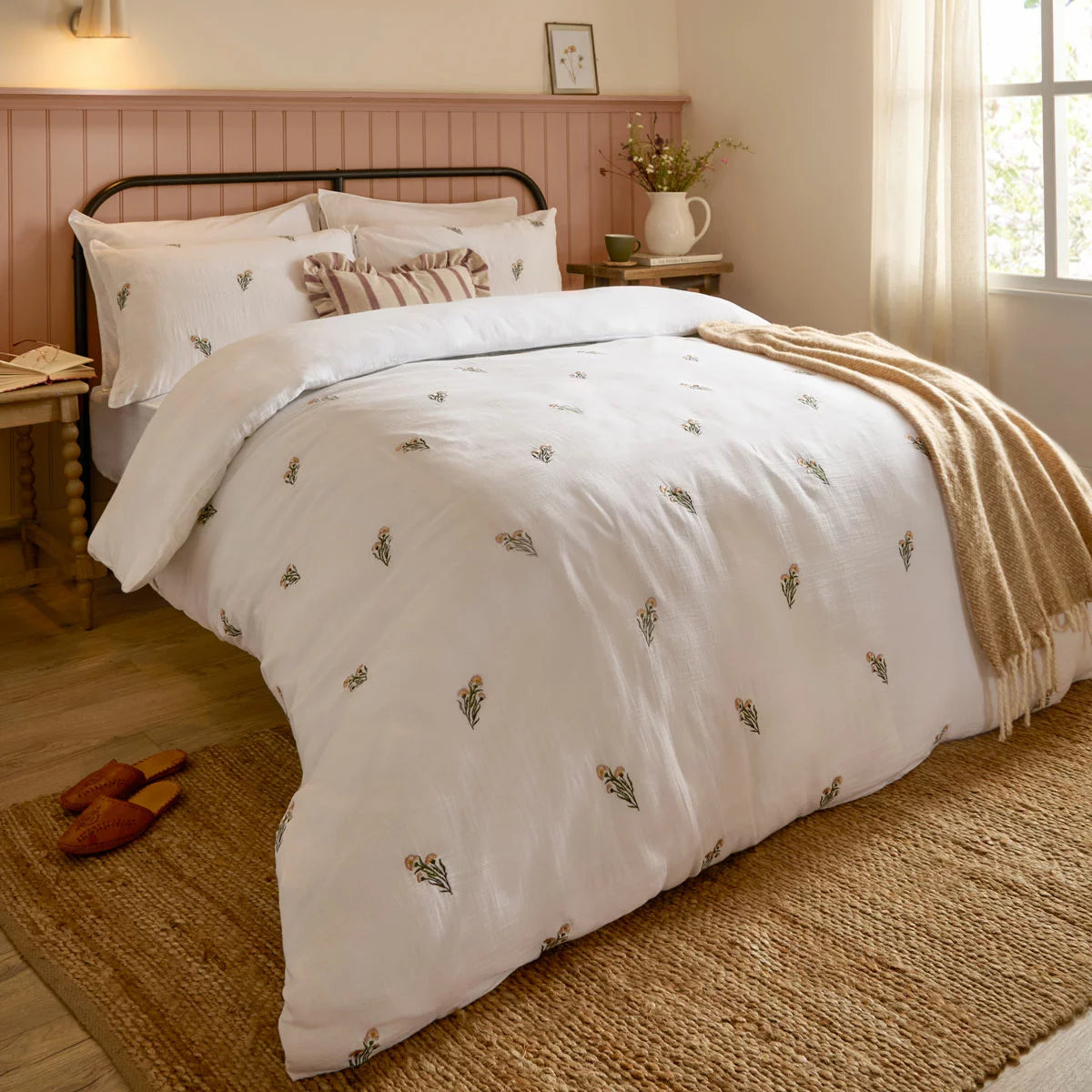 Front view of the white Wylder Josephine cotton muslin duvet cover showcasing delicate embroidered flowers and matching piped-edge pillowcases on a mattress.