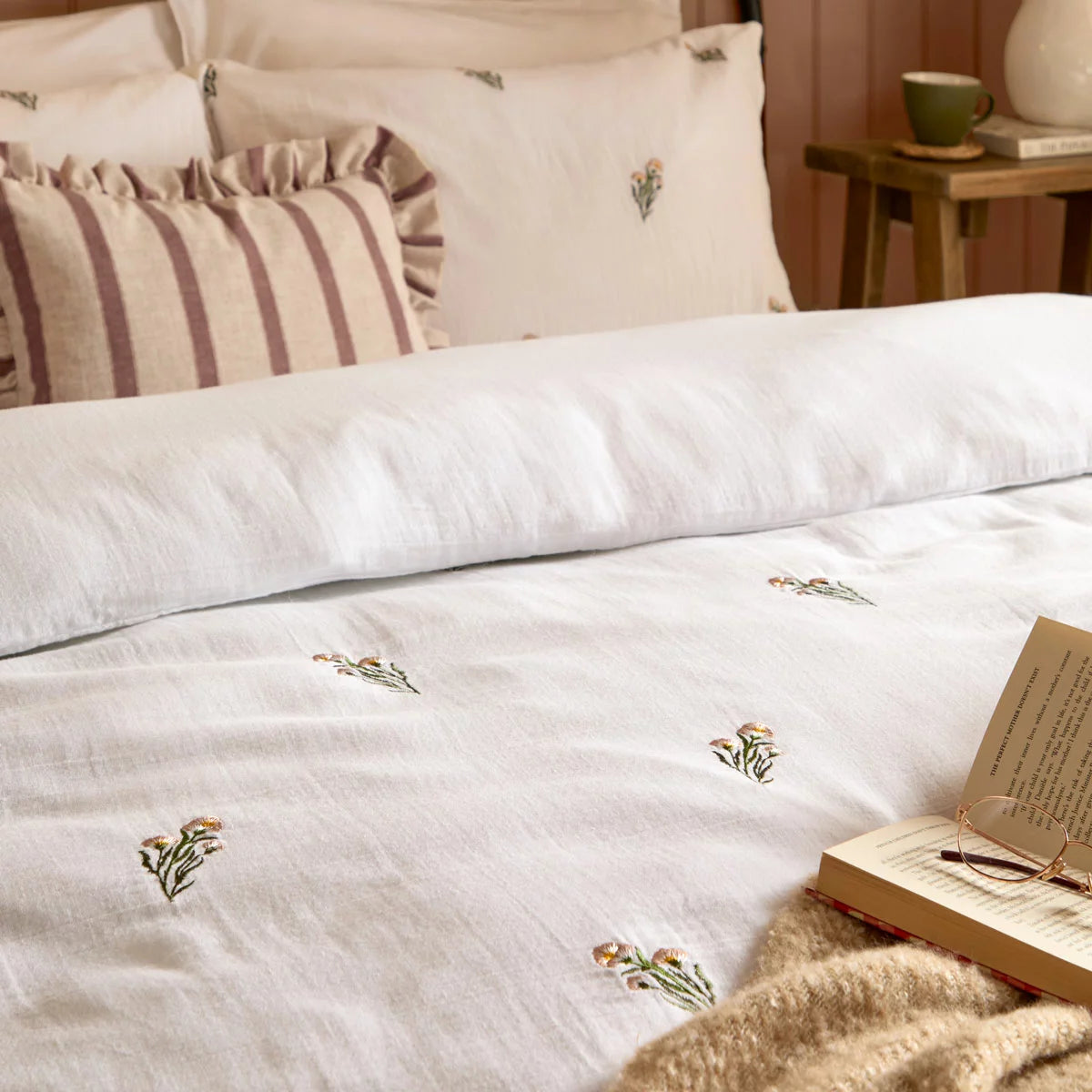 Front view of the white Wylder Josephine cotton muslin duvet cover showcasing delicate embroidered flowers and matching piped-edge pillowcases on a mattress.