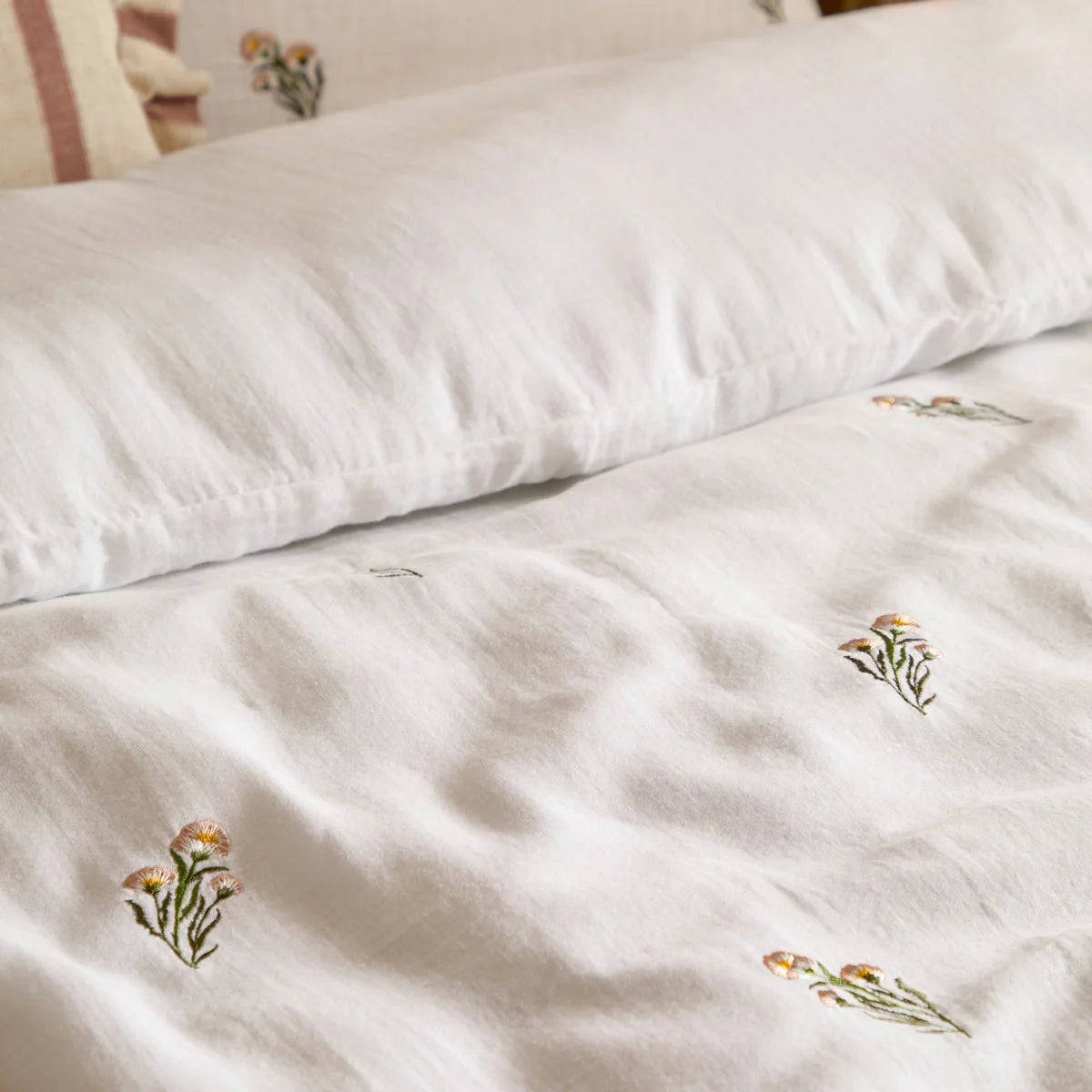Front view of the white Wylder Josephine cotton muslin duvet cover showcasing delicate embroidered flowers and matching piped-edge pillowcases on a mattress.