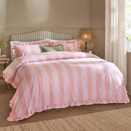 Front view of the pink and white striped Wylder Birdie duvet cover with delicate ruffle trim edges laid neatly on a bed in a bright bedroom.