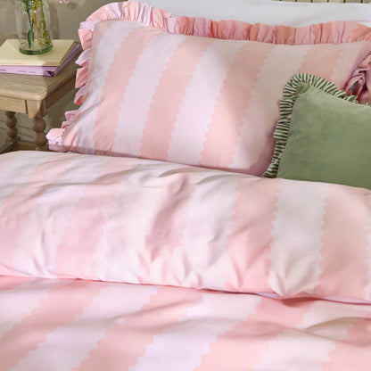 Front view of the pink and white striped Wylder Birdie duvet cover with delicate ruffle trim edges laid neatly on a bed in a bright bedroom.