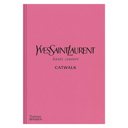 Opened hardcover book YSL Catwalk displaying vibrant runway models and descriptive text on a dark wooden tabletop.