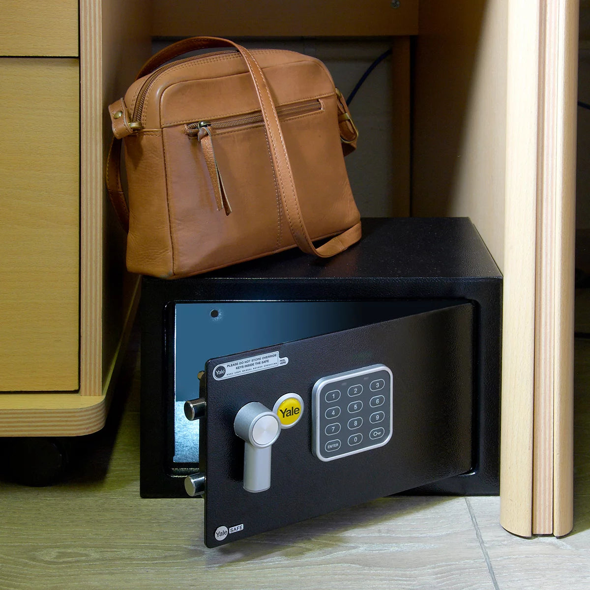 Front angle view of the black Yale 16.3L medium digital safe with electronic keypad and keyhole cover mounted on a light wood background.