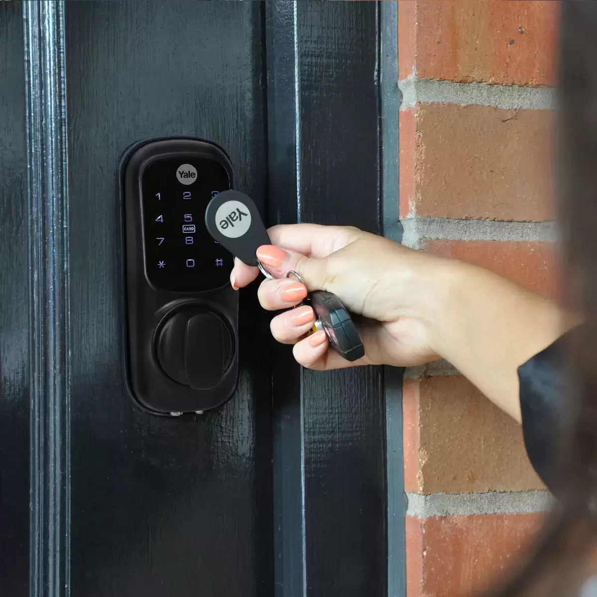 A close-up shot of the matte black Yale Keyless Smart Lock displaying illuminated blue numbers on its digital touch screen, mounted onto a modern dark oak wooden door.