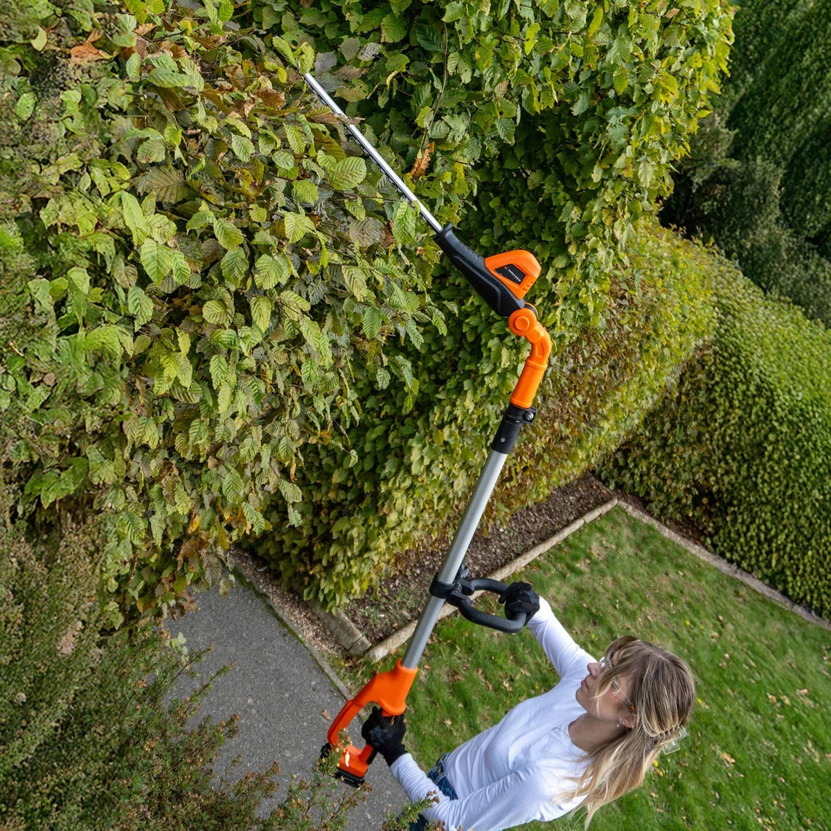 Orange and silver Yard Force 20V cordless pole hedge trimmer showing its 45cm steel blade, extended telescopic pole, and adjustable pivoting head against a garden background.