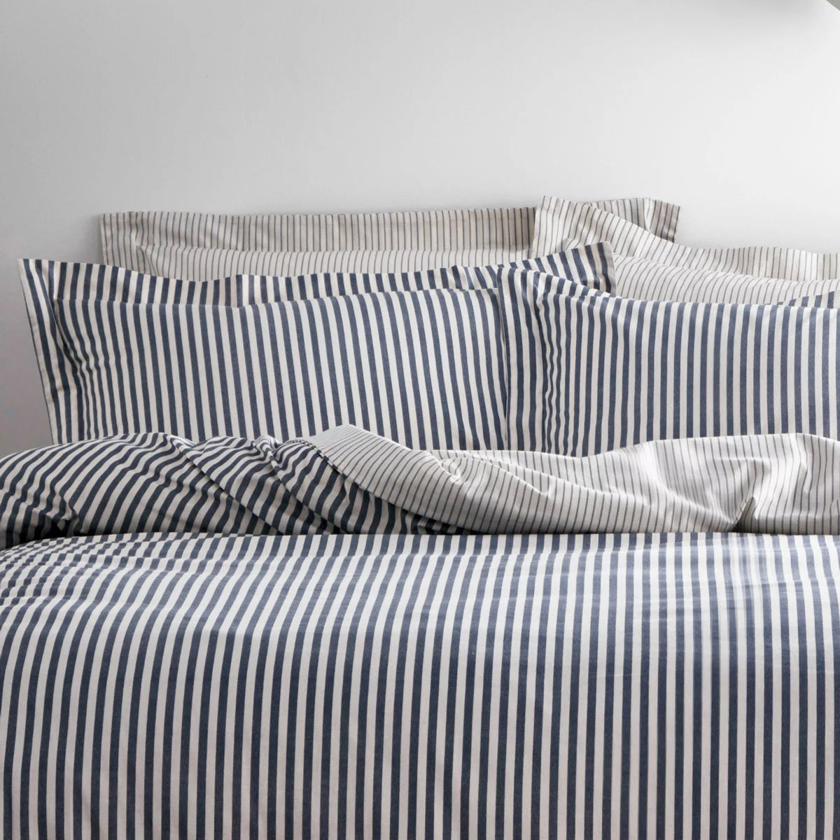 Reversible Yard Hebden navy blue and white striped cotton duvet cover neatly spread on a modern wooden bed frame within a brightly lit bedroom.