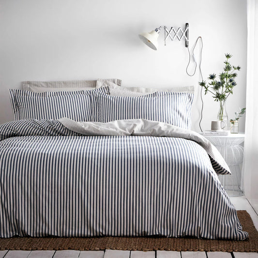 Reversible Yard Hebden navy blue and white striped cotton duvet cover neatly spread on a modern wooden bed frame within a brightly lit bedroom.