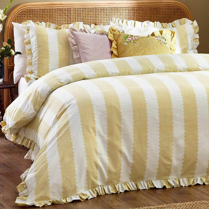 A double bed styled with the yellow-striped Wylder Birdie duvet cover, showcasing the delicate ruffled edges of the pillowcases and cover under warm bedroom lighting.