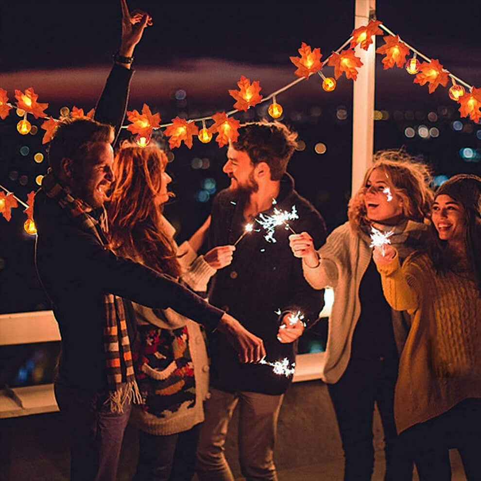 A 20 LED ZOELNIC orange maple leaf string light glowing warmly along a decorated wooden porch railing.