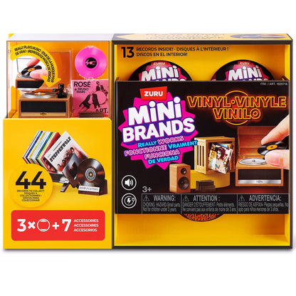 Three colorful ZURU Mini Brands mystery capsules set next to a tiny working black and red mini record player with mini vinyl records spread across a white surface.