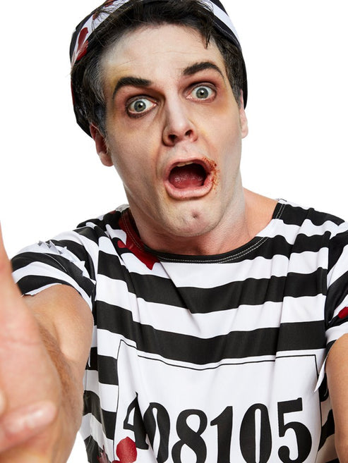 Front view of adult wearing a tattered black and white striped zombie convict costume with bloody splatters in a dimly lit studio setting.