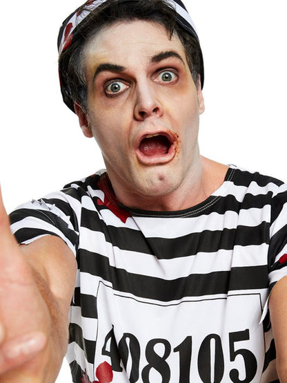 Front view of adult wearing a tattered black and white striped zombie convict costume with bloody splatters in a dimly lit studio setting.