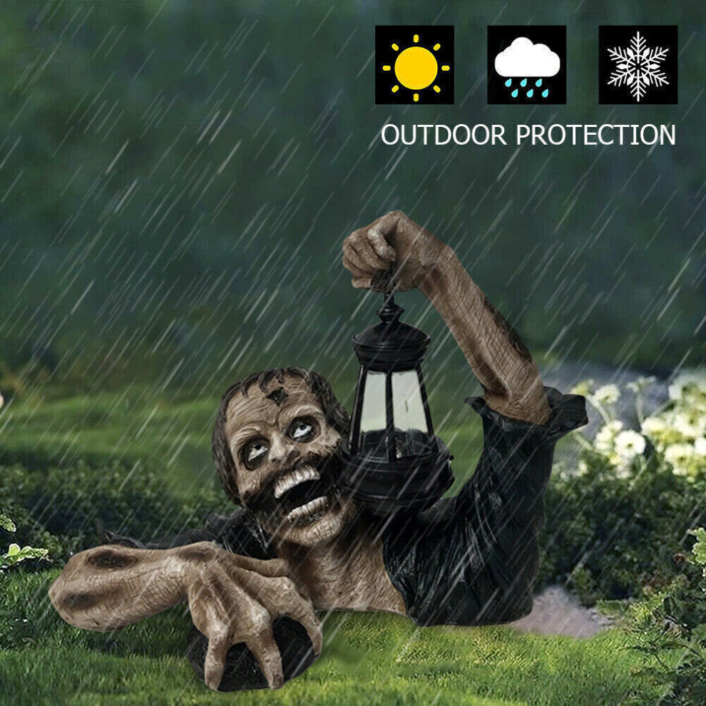 A resin zombie crawling out of a grave holding a glowing LED lantern garden statue, positioned among autumn leaves for a spooky Halloween display.