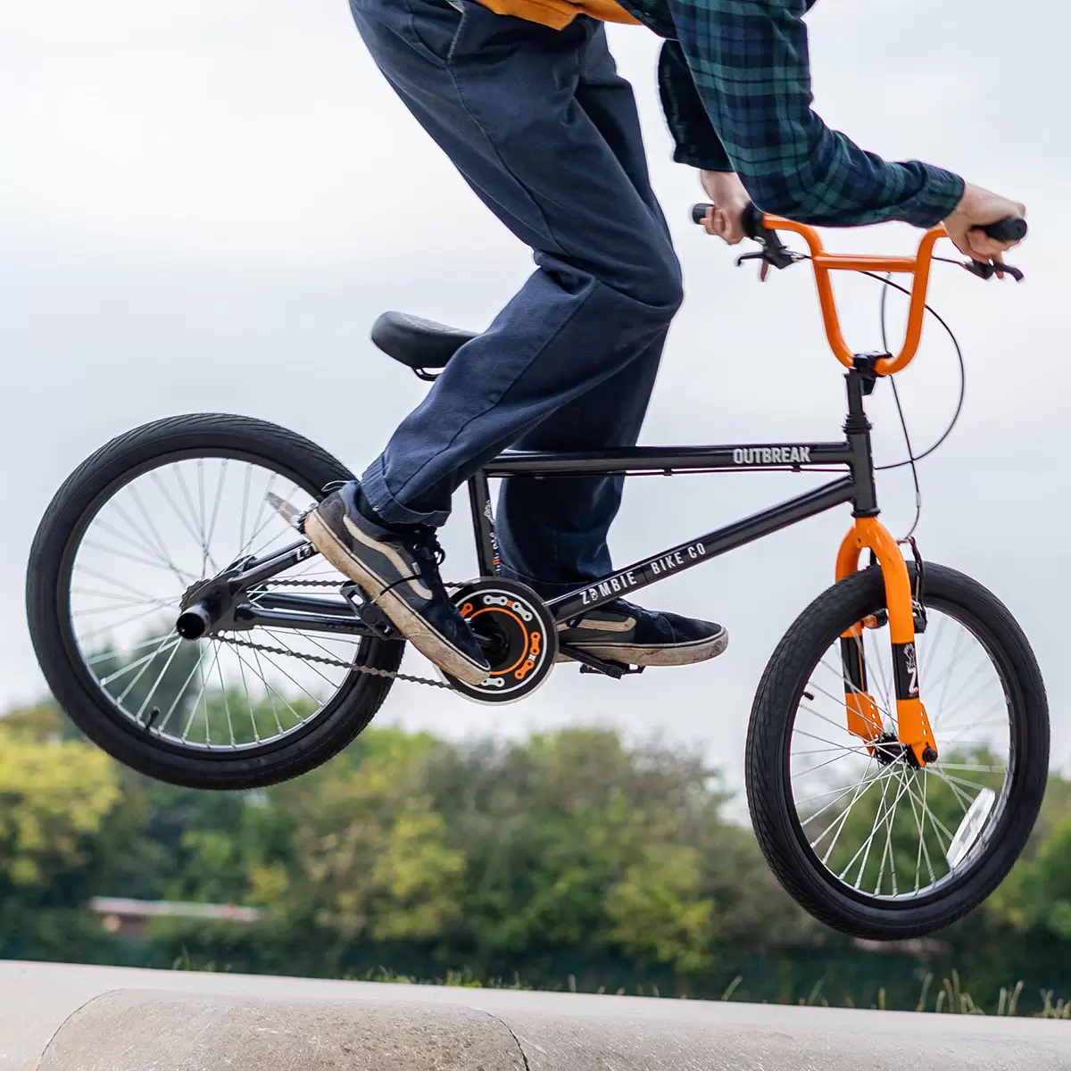 Side angle profile of the grey Zombie Outbreak 20-inch wheel BMX bike with black grips, alloy wheels, and installed front stunt peg on a concrete skatepark surface.