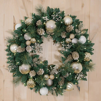 Front view of a 30-inch pre-lit holiday wreath with dense green faux pine needles, natural pinecones, red ornaments, and 50 glowing warm white LEDs displayed on a dark wooden front door.