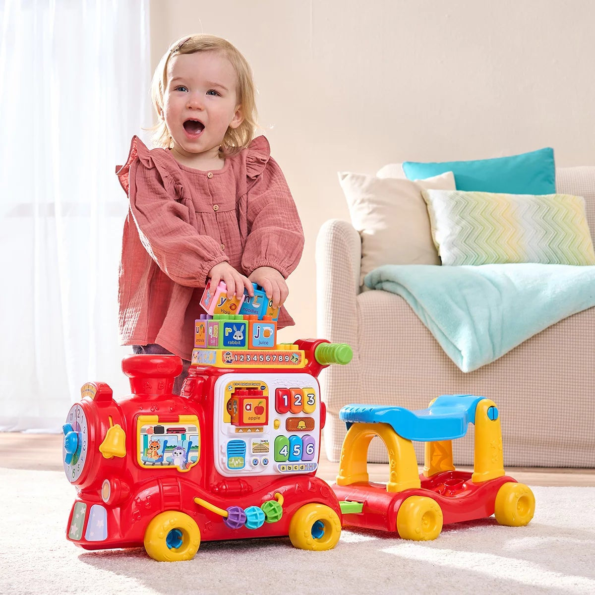 Side view of the bright red and yellow plastic VTech 4-in-1 Alphabet Express train showing the floor-play block reader, ride-on seat, and interactive light-up buttons on a plain white studio background.