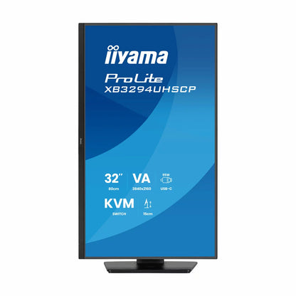A sleek matte black 32-inch iiyama ProLite 4K professional monitor with thin bezels sits on a minimalist wooden office desk, showcasing a crisp multi-window data layout in a bright studio.