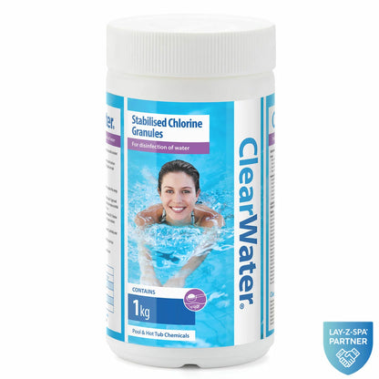 Six 1kg white tub containers of Clearwater stabilised chlorine granules grouped together on a grey stone patio beside a clear outdoor hot tub.