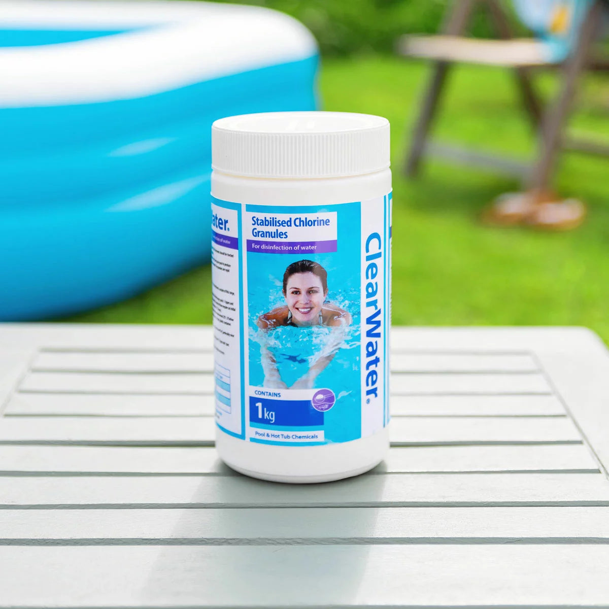 Six 1kg white tub containers of Clearwater stabilised chlorine granules grouped together on a grey stone patio beside a clear outdoor hot tub.