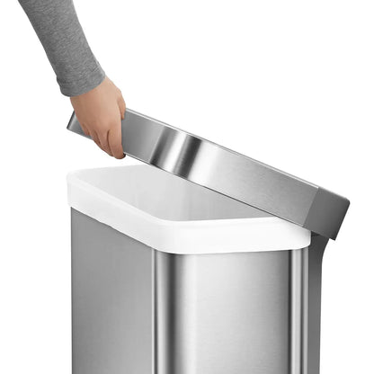 Front angle view of the simplehuman 55L brushed stainless steel step bin with grey plastic lid set against a bright modern kitchen backdrop.