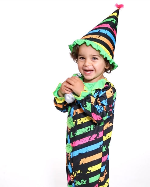 A child wearing a spooky Little Funhouse Clown jumpsuit and matching pointed clown hat standing in a Halloween setting.